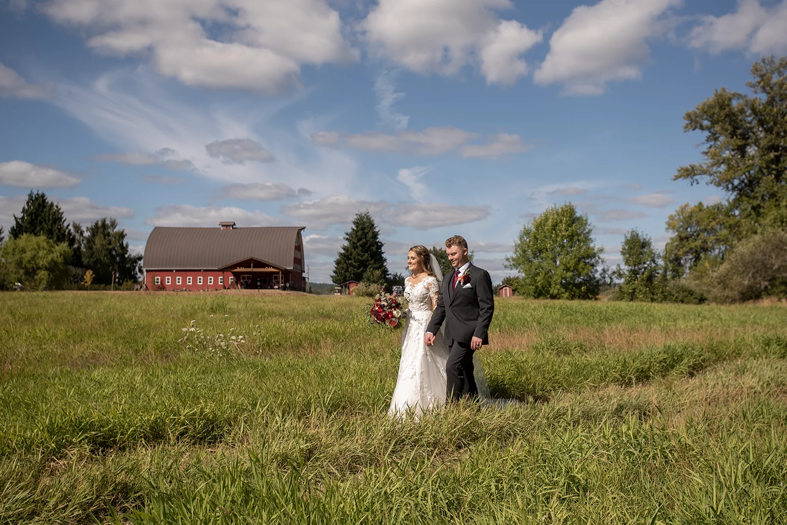 A bride and groom walk hand-in-hand to a ceremony site in the back field at Red Barn Studios in Chehalis, WA.